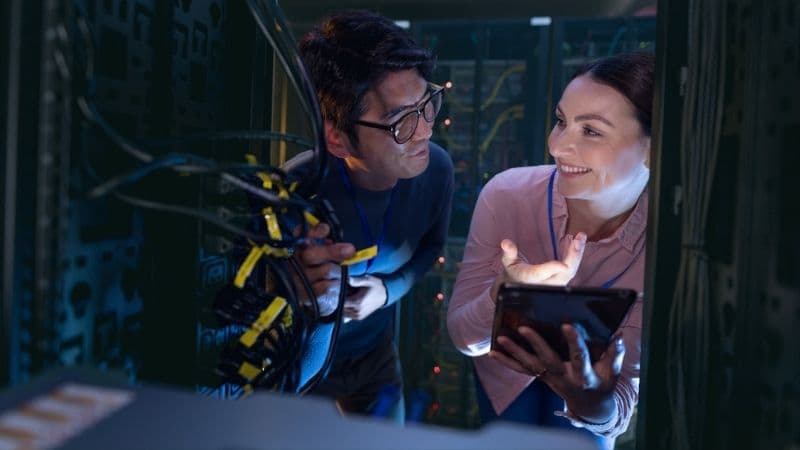 Male And Female Engineers With Digital Tablet Inspecting The Server In Computer Server Room. Database Server Management And Maintenance Concept